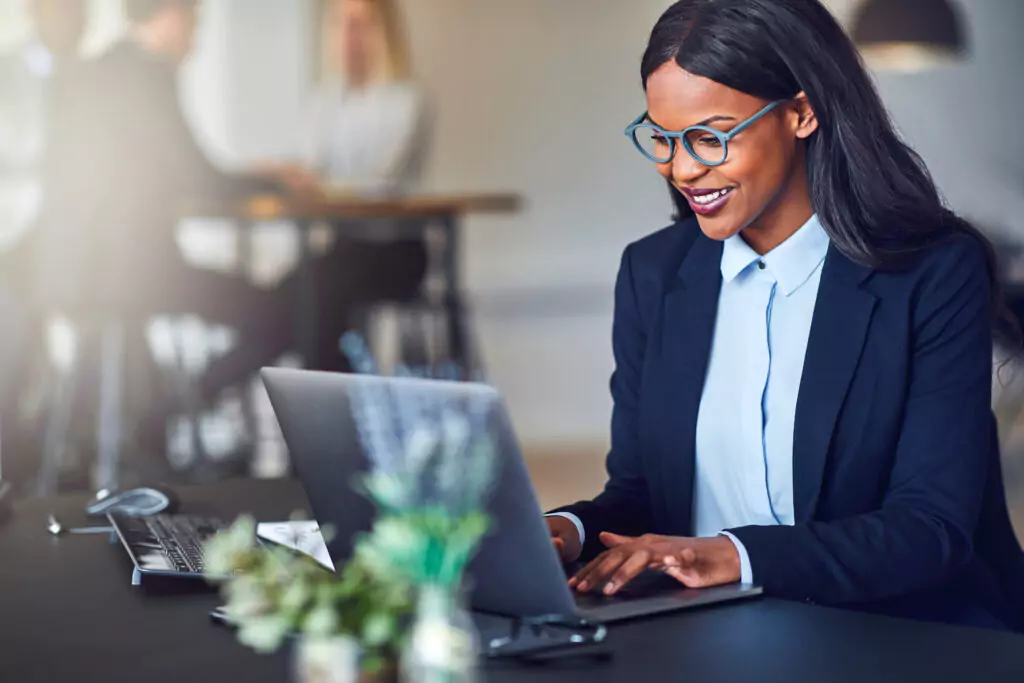 woman with glasses using laptop and smiling