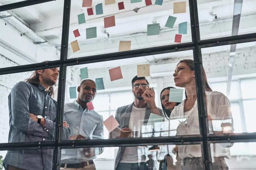 a group of people in an office writing on post-its and sticking them to a glass wall