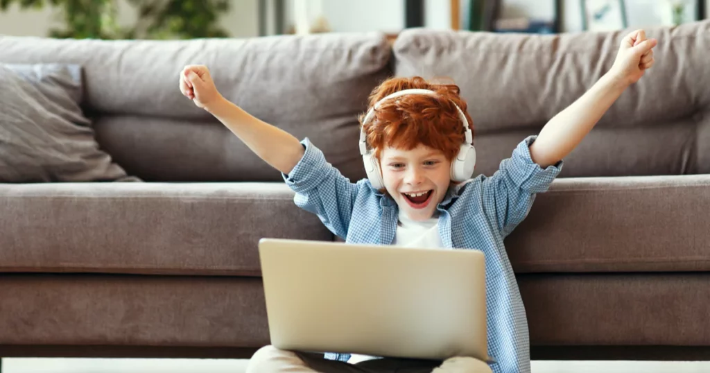 redheaded boy cheering while using a laptop