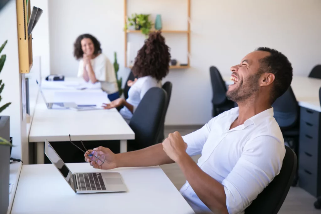 Man laughing in front of laptop inside an office
