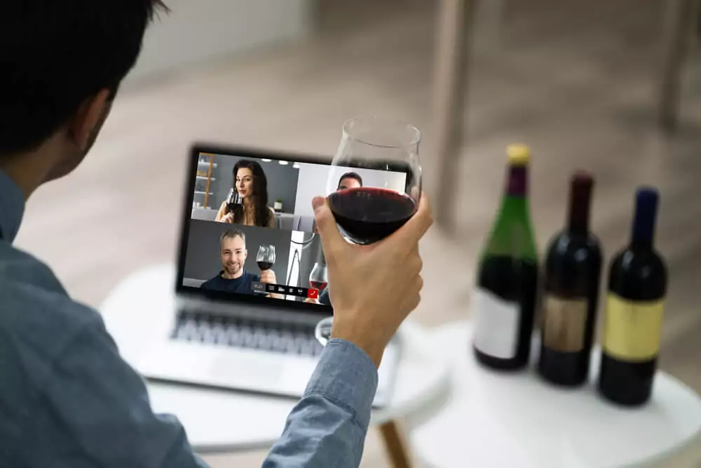 a man in a virtual meeting holding a glass of wine