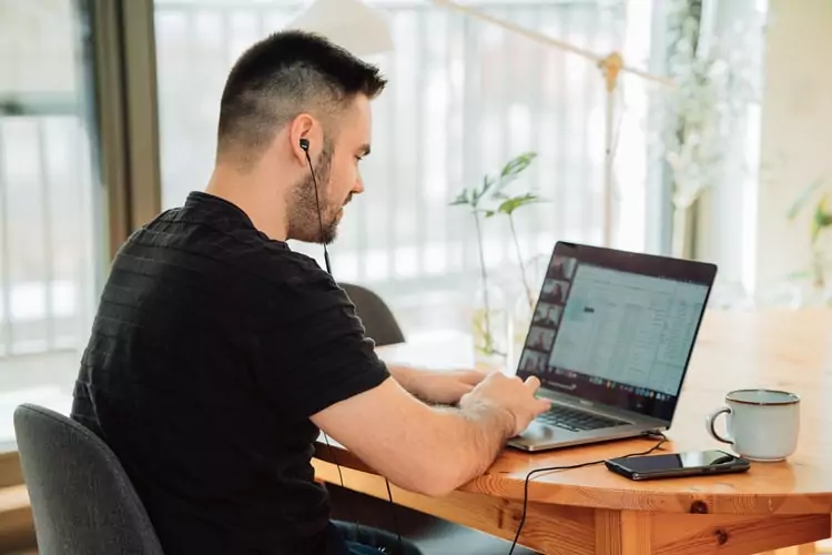 a man sitting at a table with a cup of coffee participating in a virtual meeting