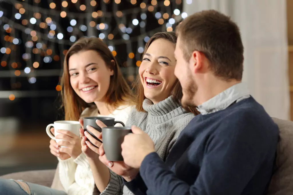 three people sitting together laughing and holding coffee mugs