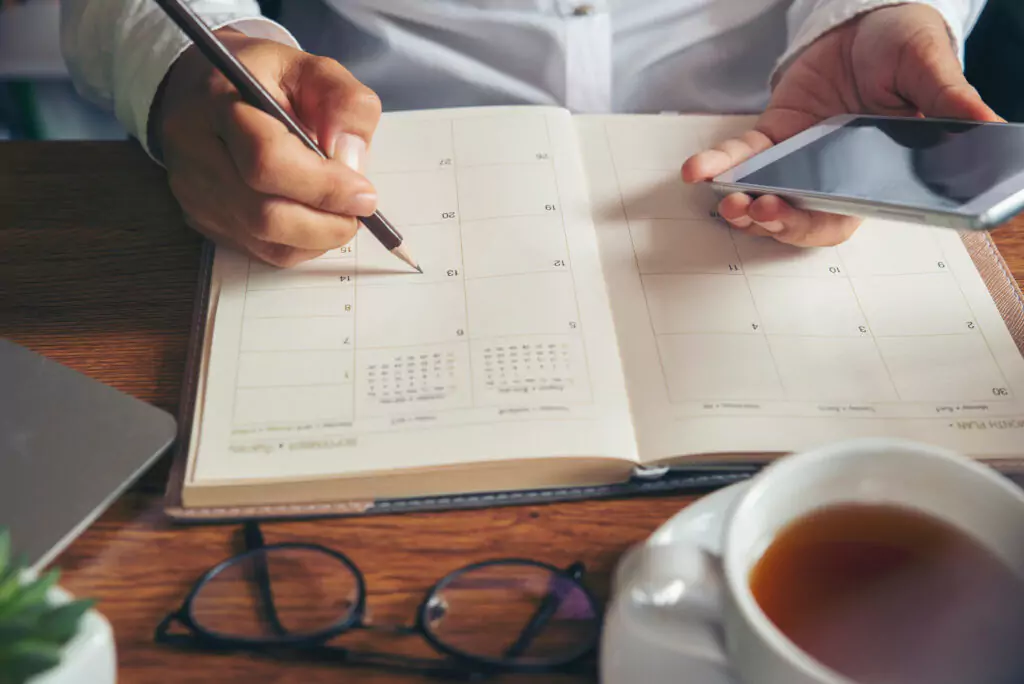 Man hands and a planner with a pencil and phone