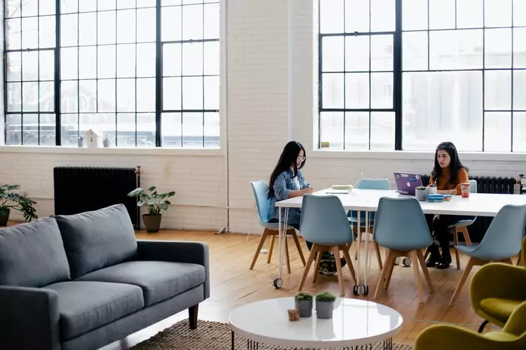 two women working separately at a communal table in a large office