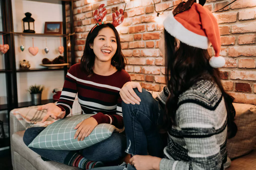 two young women sitting on a couch talking and wearing Christmas themed clothes