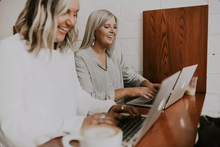 two women using laptops at a desk together