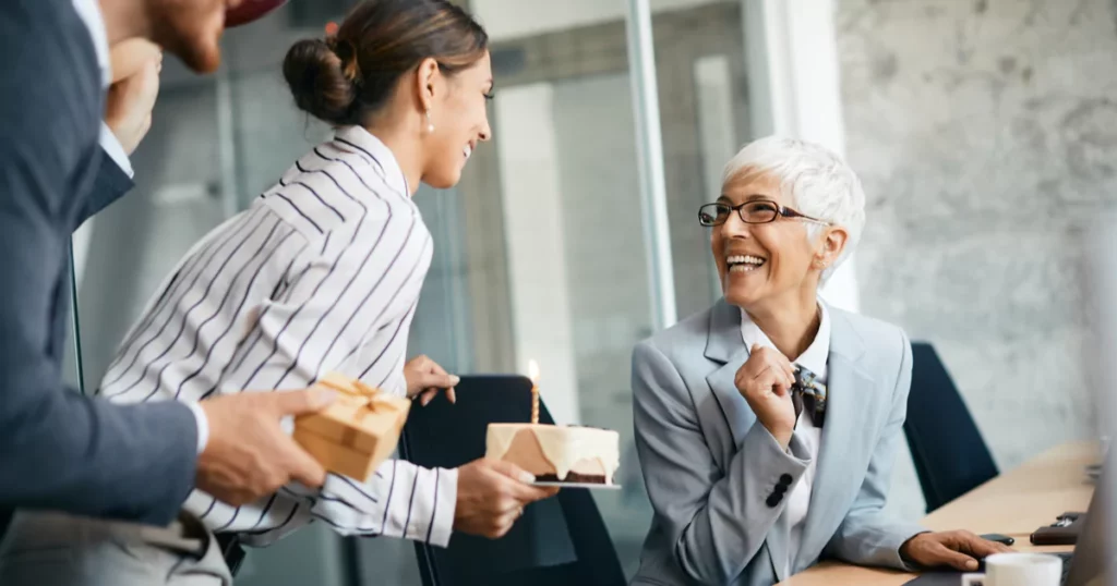 https://teambuildinghub.com/wp-content/uploads/2022/06/coworkers-cake-smile-retirement-party-1024x538.webp